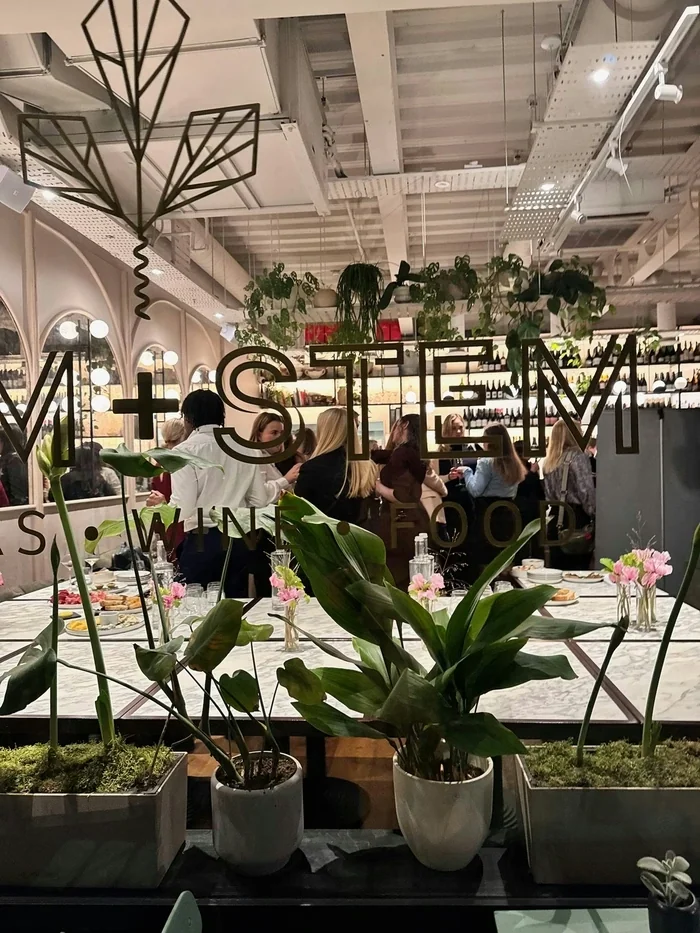 Dining room with plants, floral table settings and guests gathered around a restaurant bar